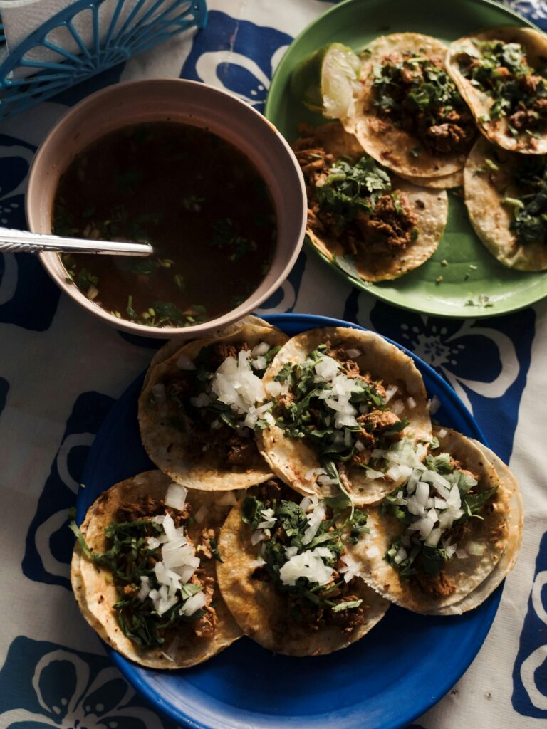 A plate of crispy birria tacos with rich consommé on the side for dipping.