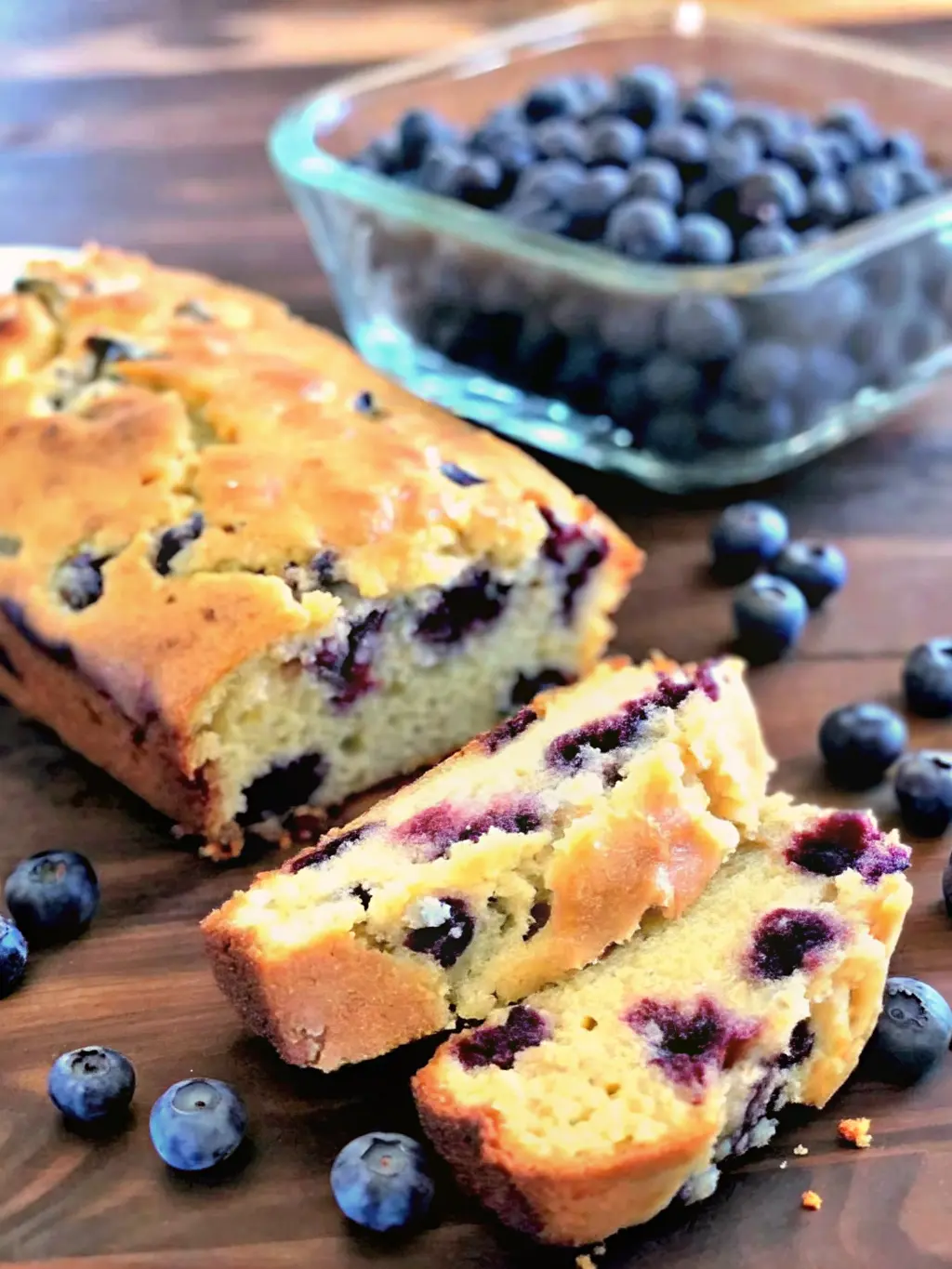 A single, perfect slice of Blueberry Cream Cheese Loaf, showcasing its moist, tender crumb with distinct purple blueberries and creamy white swirls, sitting on a minimalist white plate. The golden crust is visible. A blurred loaf is in the background. Taken on a white marble countertop with natural morning light, soft shadows, warm tones. NO HANDS OR PEOPLE.