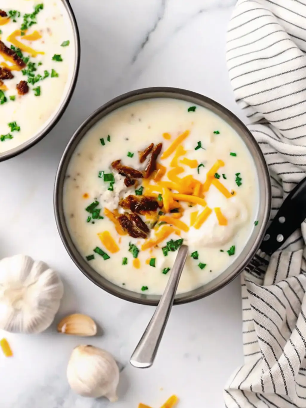 Close-up, overhead shot of key ingredients for Creamy Vegan Loaded Baked Potato Soup laid out on a clean white marble countertop. This includes peeled and cubed russet potatoes, a bowl of pre-soaked cashews, fresh garlic cloves next to a whole garlic bulb, a bottle of vegetable broth, and fresh chives on a rustic wooden cutting board. Natural morning light creates soft shadows. Warm tones, clean and tidy presentation. NO HANDS. (3:4 ratio)