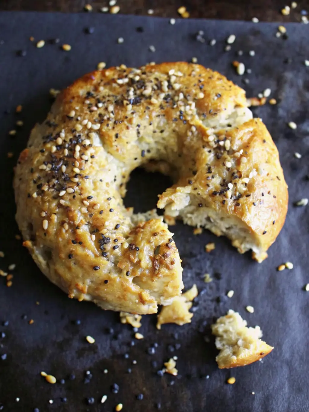 A Greek Yogurt Bagel, sliced in half horizontally, revealing its airy, chewy texture. One half is lightly toasted and spread with cream cheese, garnished with a sprig of fresh dill. It rests on a minimalist white plate on a marble countertop, with subtle wood accents. Natural morning light, warm tones. NO HANDS OR PEOPLE.