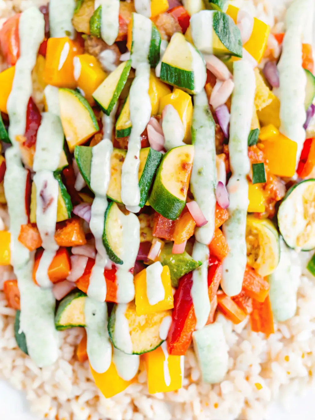 A medium shot of diced, colorful roasted vegetables (zucchini, red bell pepper, yellow bell pepper, red onion) just out of the oven, lightly caramelized and glistening, being gently tossed on a baking sheet. A small blender with blended pale green Green Onion Cashew Sauce in the foreground, slightly out of focus. The scene is on a white marble countertop with natural morning light, soft shadows, and warm tones. NO HANDS.