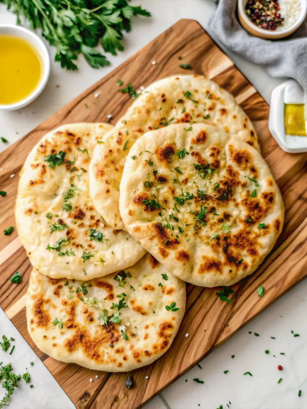 A detailed shot highlighting the tender, airy texture of a Fluffy Cottage Cheese Flatbread, broken slightly to reveal its fluffy interior. It's resting on the wooden cutting board, garnished with olive oil and fresh parsley. A full stack of flatbreads is blurred in the background, on the marble countertop. Natural morning light, soft shadows, warm tones, clean and tidy, no hands or people. (3:4 ratio)