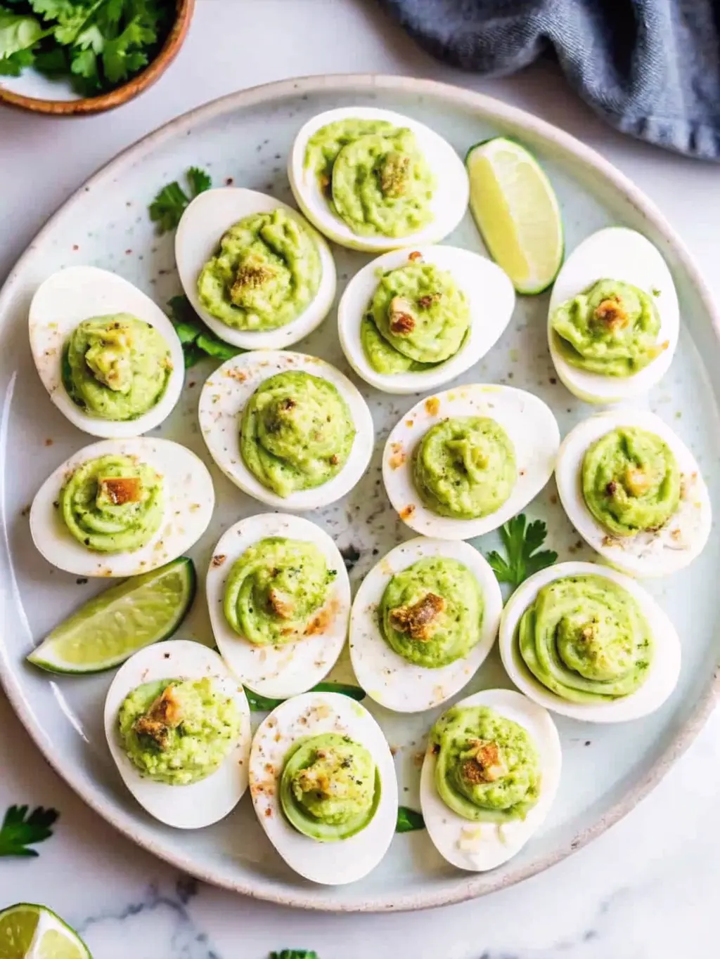 Close-up shot emphasizing the creamy texture and presentation of several finished 'Million Dollar Deviled Eggs' on a minimalist blue-grey ceramic plate. The golden-yellow piped filling shows a smooth, rich consistency, beautifully contrasted by the vibrant red paprika dust and green chives. The background features a subtle hint of fresh green herbs in a ceramic pot and a wooden accent. Natural morning light creates inviting soft shadows and warm tones on the marble countertop, highlighting the clean and tidy presentation. 3:4 ratio. NO HANDS OR PEOPLE.