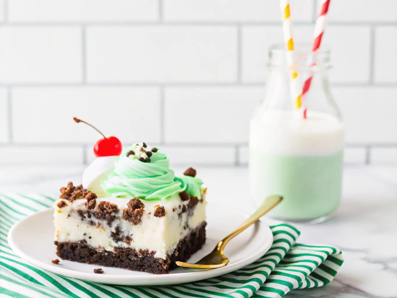 A generous slice of St. Patrick's Day Shamrock Lasagna dessert on a minimalist white plate, showcasing distinct layers of dark Oreo crust, light cream cheese, and vibrant mint green, topped with fluffy white whipped cream, crushed Oreos, green sprinkles, and a bright red maraschino cherry. A golden fork rests beside the plate on a yellow and white striped linen. A glass bottle of milk with a blue striped straw is in the soft focus background. Shot with natural morning light from an east window, soft shadows, warm tones, clean marble countertop with subtle wood accents in the distance. No hands or people. (4:3 ratio)