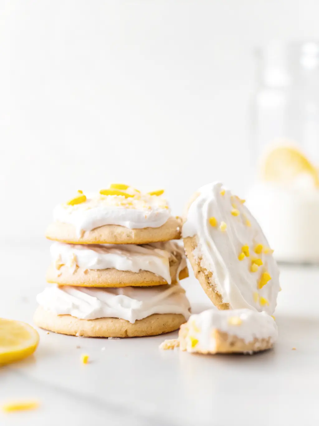 Ingredients for soft-baked vegan lemon cookies: fresh lemons, a bowl of gluten-free 1:1 baking flour, a stick of vegan butter, a jar of applesauce, and granulated sugar. All arranged on the same wooden cutting board on a white marble countertop, bathed in natural morning light. Soft shadows, warm tones, clean and tidy presentation. 3:4 ratio. NO HANDS.