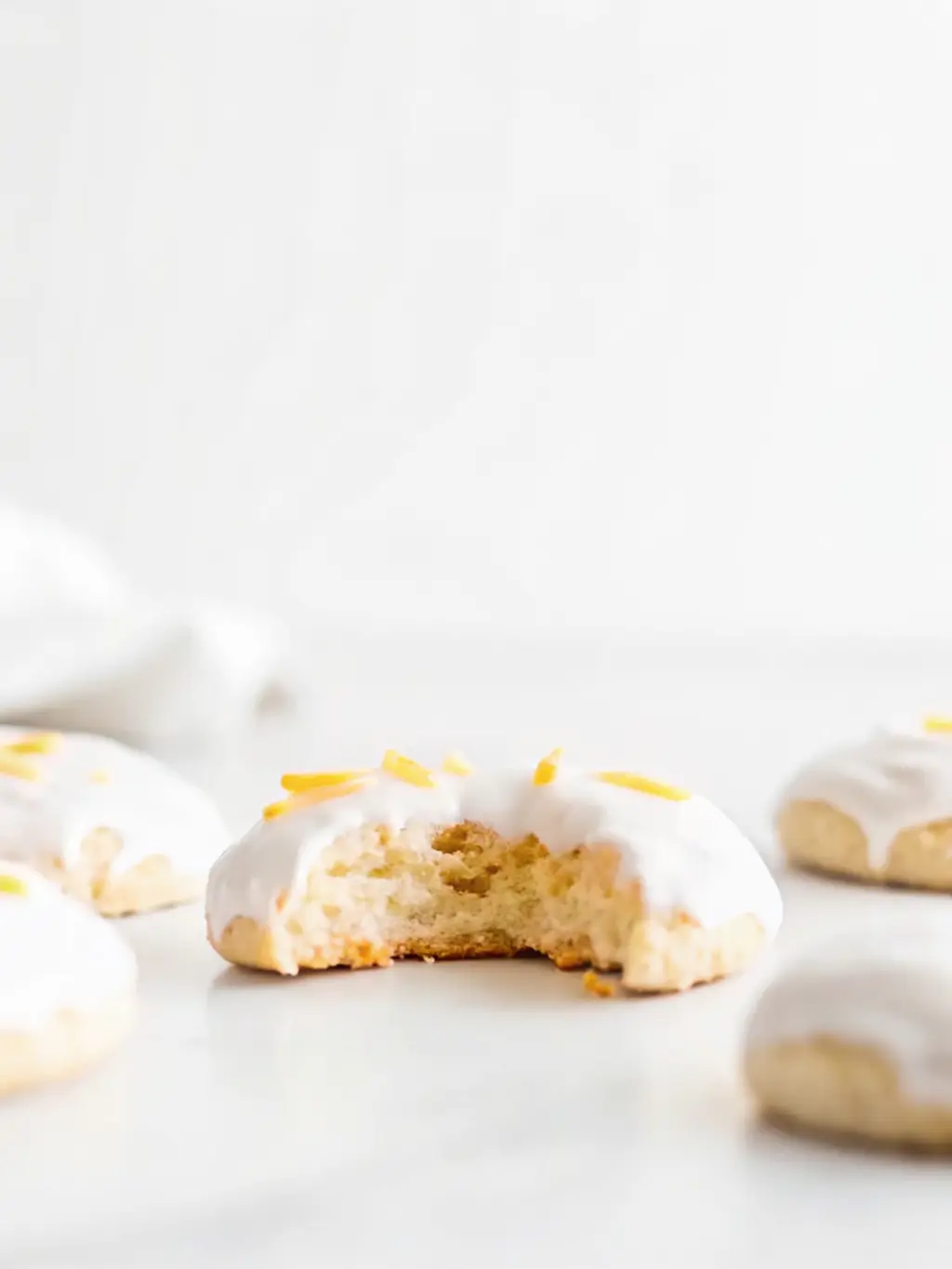 A close-up of the vegan lemon cookie dough being scooped onto a parchment-lined baking sheet, showcasing its soft, pliable texture. A wooden spoon or cookie scoop is visible. The scene is on a white marble countertop with wood accents in the background, under natural morning light. Soft shadows, warm tones, clean and tidy presentation. 3:4 ratio. NO HANDS.