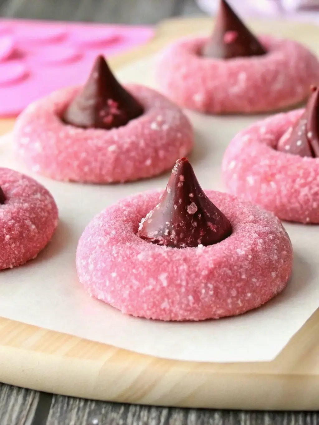Close-up of ingredients for Strawberry Kiss Cookies laid out on a marble countertop. Softened butter in a minimalist white ceramic bowl, flour in another, a bottle of strawberry extract, and a few unwrapped Hershey's Kisses. The wooden cutting board is subtly visible, and fresh herbs are in the background, all illuminated by soft morning light. (3:4 ratio) NO HANDS OR PEOPLE.