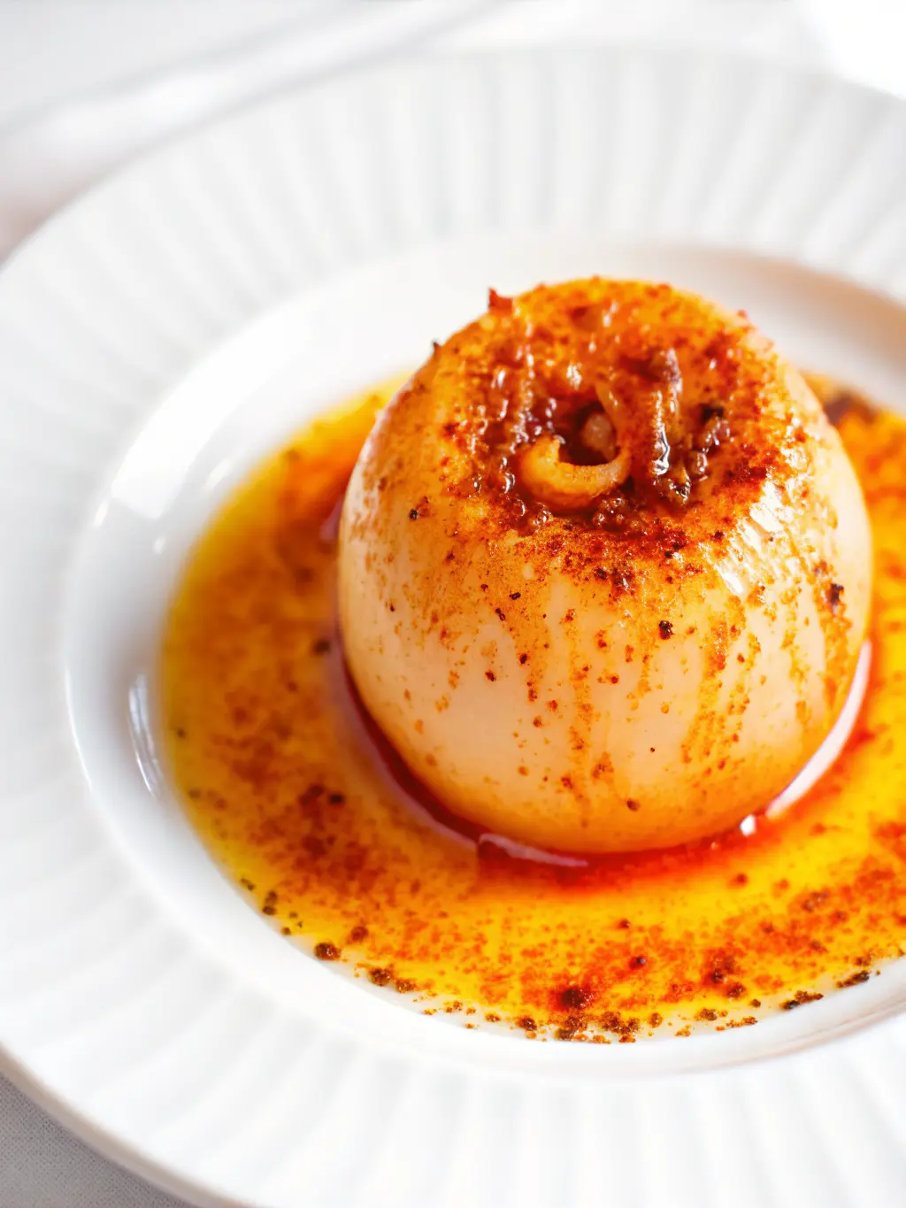 A close-up shot of a single whole onion gently simmering in a stainless steel pot filled with clear liquid, steam subtly rising. The pot is on a burner (subtly visible), on a marble countertop. Focus is on the onion's translucent layers as it cooks. Natural morning light, soft shadows, warm tones, clean and tidy kitchen environment. No hands or people. (3:4 ratio)