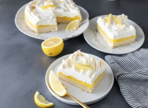 Hero shot of a square slice of Lemon Lush Cake on a minimalist white ceramic plate. The cake shows distinct layers: a golden pecan crust at the bottom, a white cream cheese layer, a bright yellow lemon pudding layer, and a fluffy white whipped topping. A fresh lemon slice wedge and zest garnish the top. The plate sits on a marble countertop with wood accents. Natural morning light from the east creates soft shadows. In the background, a blur of fresh mint herbs. High resolution, food photography.
