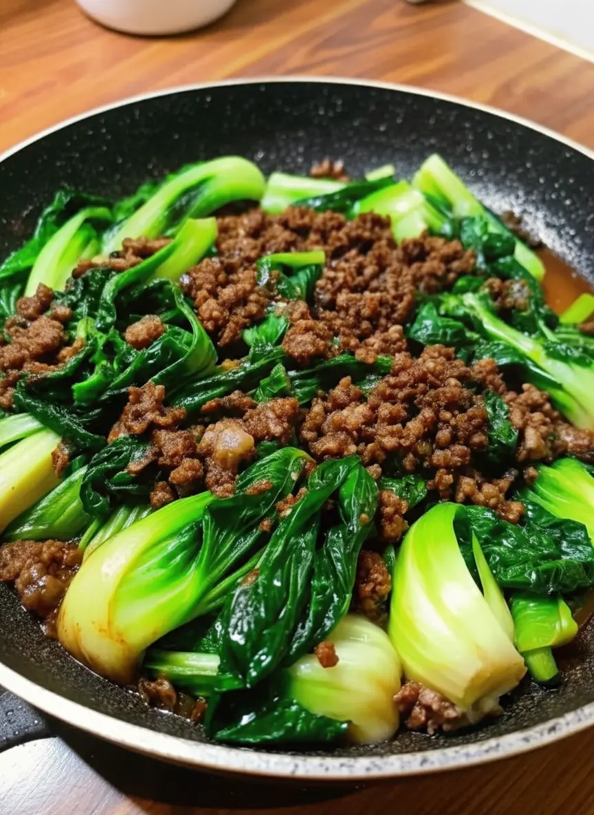 Ingredients preparation shot on a wooden cutting board sitting on a marble counter. Fresh baby bok choy halved lengthwise, raw ground beef in a ceramic bowl, minced garlic, and a small jar of oyster sauce. Natural lighting, clean and tidy presentation.