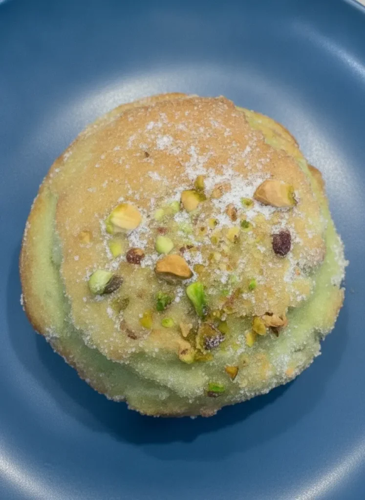 Easy Bakery-Style Pistachio Muffins - Prep focus: A rustic wooden cutting board on a white marble countertop holds a ceramic bowl filled with finely ground raw green pistachio flour next to a small bowl of whole green pistachios. Soft morning light from an east window illuminates the scene, creating gentle shadows. Clean presentation, no hands, no people.