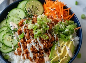 A high-angle hero shot of a High-Protein Ground Turkey Rice Bowl served in a vibrant orange ceramic bowl. The bowl contains fluffy white jasmine rice topped with savory browned ground turkey crumbles, thin slices of English cucumber, bright orange shredded carrots, and perfectly fanned avocado slices. A zig-zag drizzle of creamy white sriracha mayo covers the center, sprinkled with black and white sesame seeds and sliced green onions. The bowl sits on a white marble countertop with soft morning light from an east window casting gentle shadows. A wooden cutting board and a sprig of fresh cilantro are visible in the background.