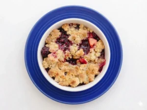 A hero shot of a golden-brown Apple and Blackberry Crumble in a white ceramic dish, placed on a marble countertop with soft morning light from an east window. A gold spoon is lifting a generous portion, revealing the dark purple blackberries and softened red-skinned apples underneath. Warm tones and soft shadows, fresh herbs in a small pot in the background. 4:3 ratio.